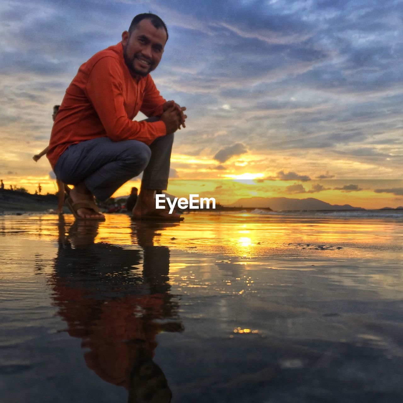 Full length of man crouching on beach during sunset