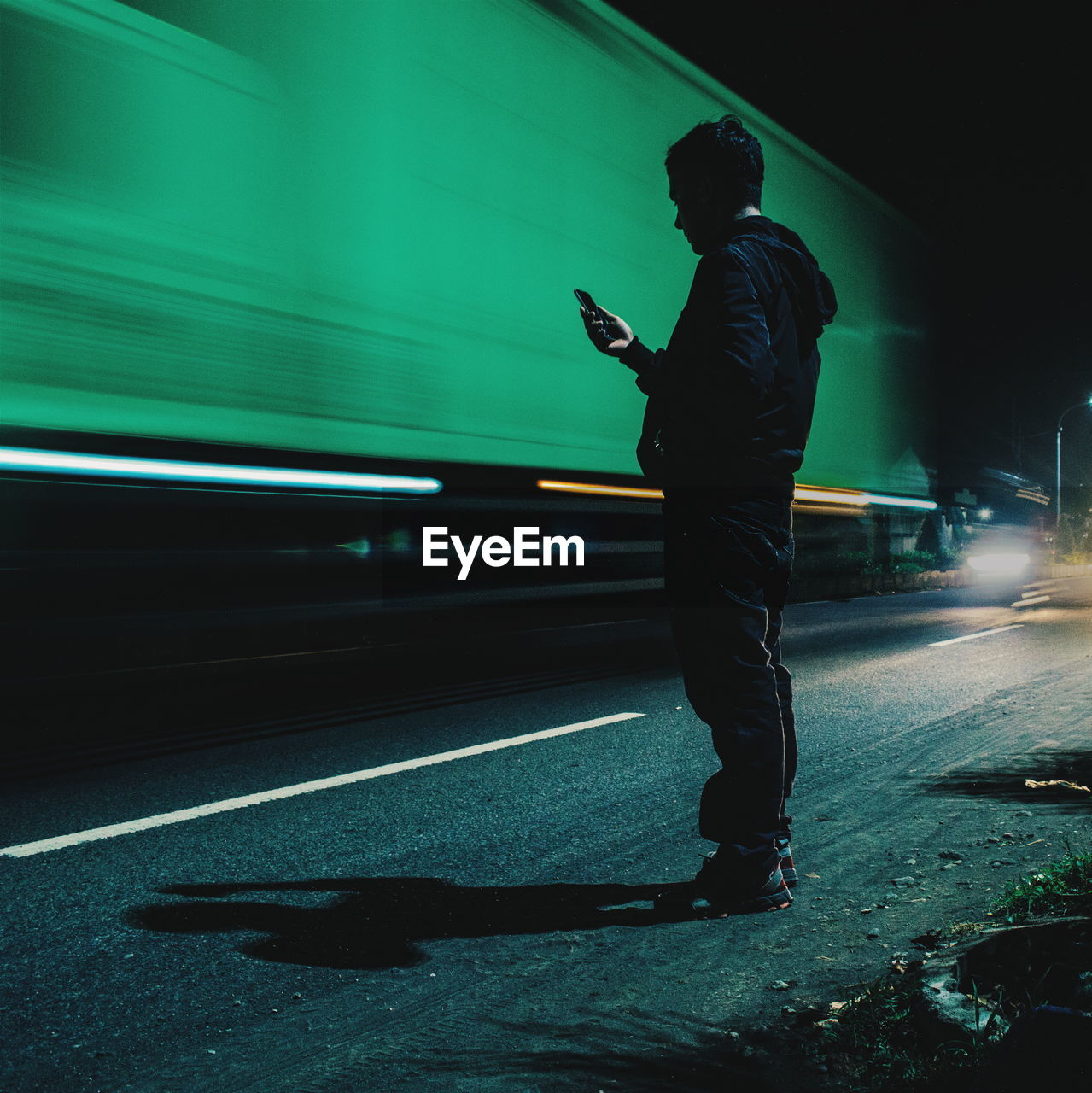 Man using phone by blurred motion of truck on road at night