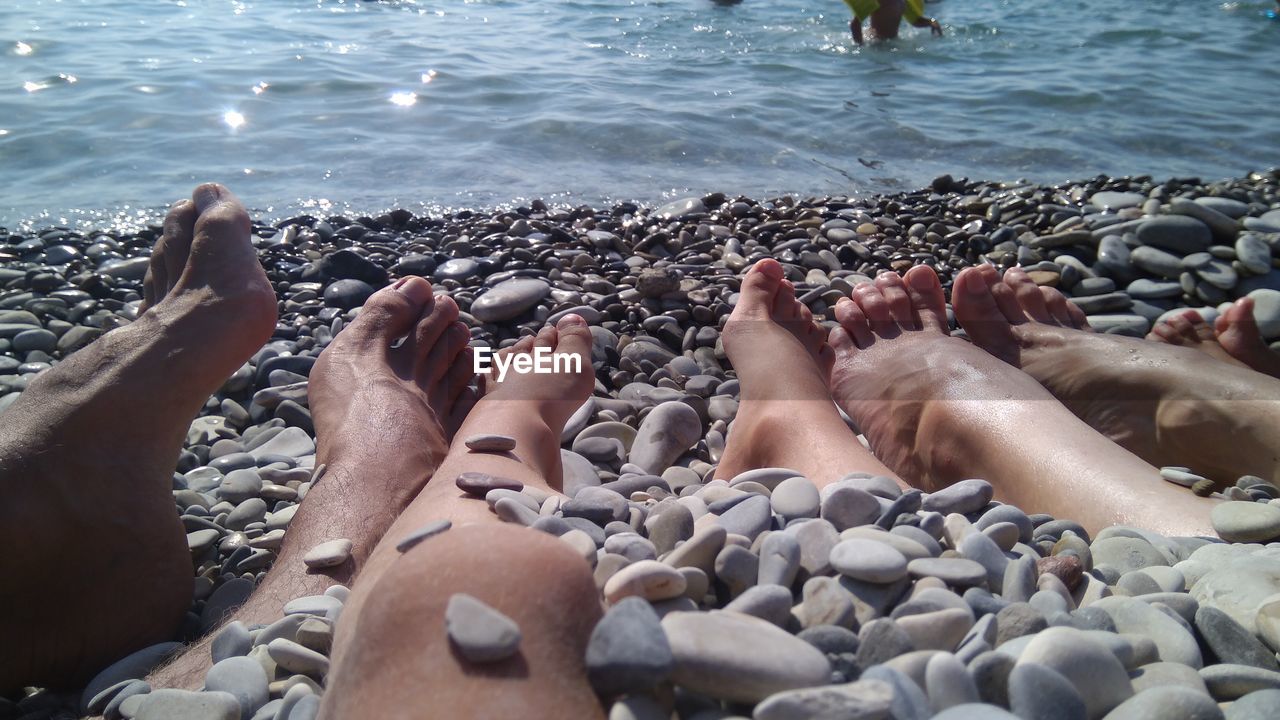 LOW SECTION OF PERSON RELAXING ON PEBBLES AT SEA