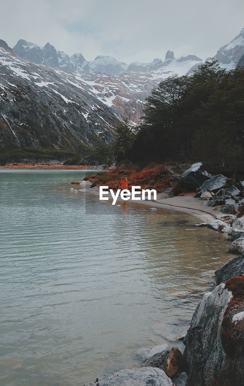 Person walking by lake against snowcapped mountains