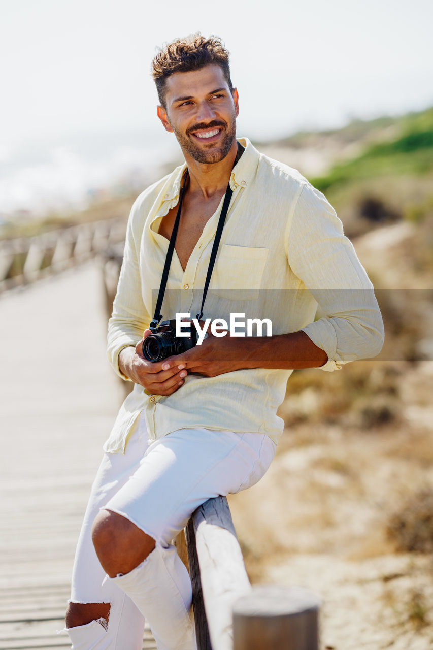 Smiling man with camera looking away while standing by railing