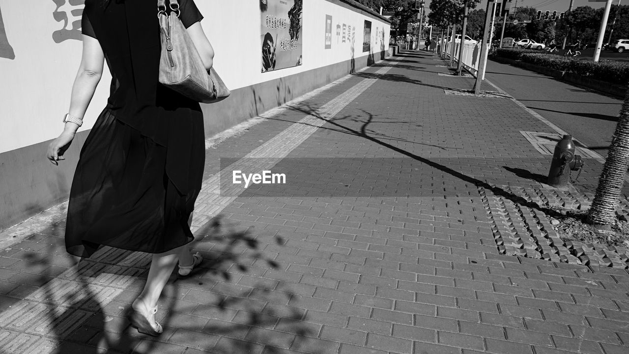 LOW SECTION OF WOMAN WALKING ON COBBLESTONE STREET