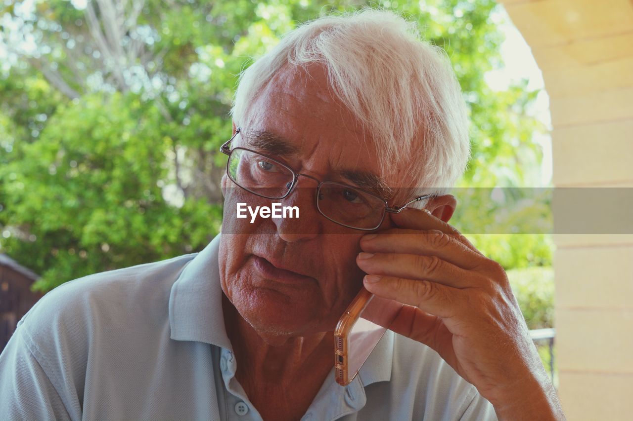 Close-up of senior man looking away while answering smart phone