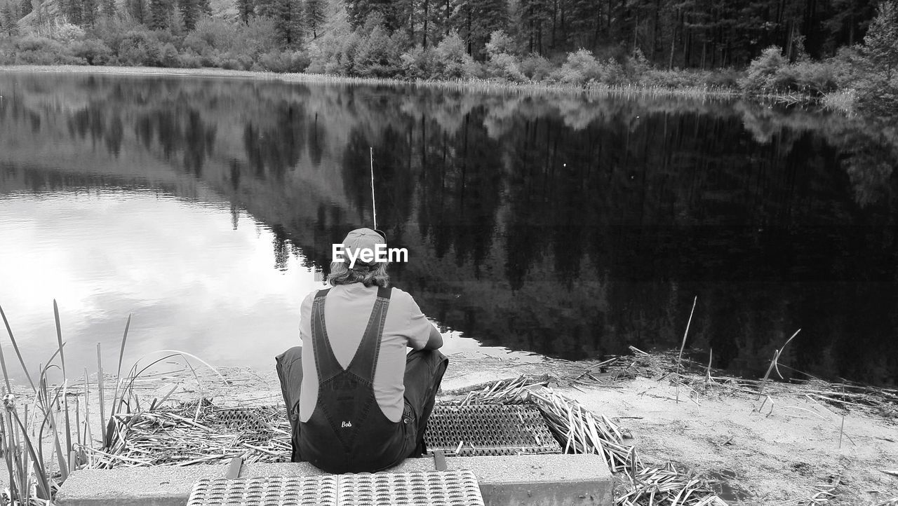 Rear view of man fishing while sitting at lakeshore