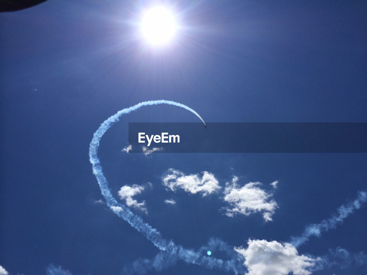 Low angle view of airplane with trail in flight against the sun