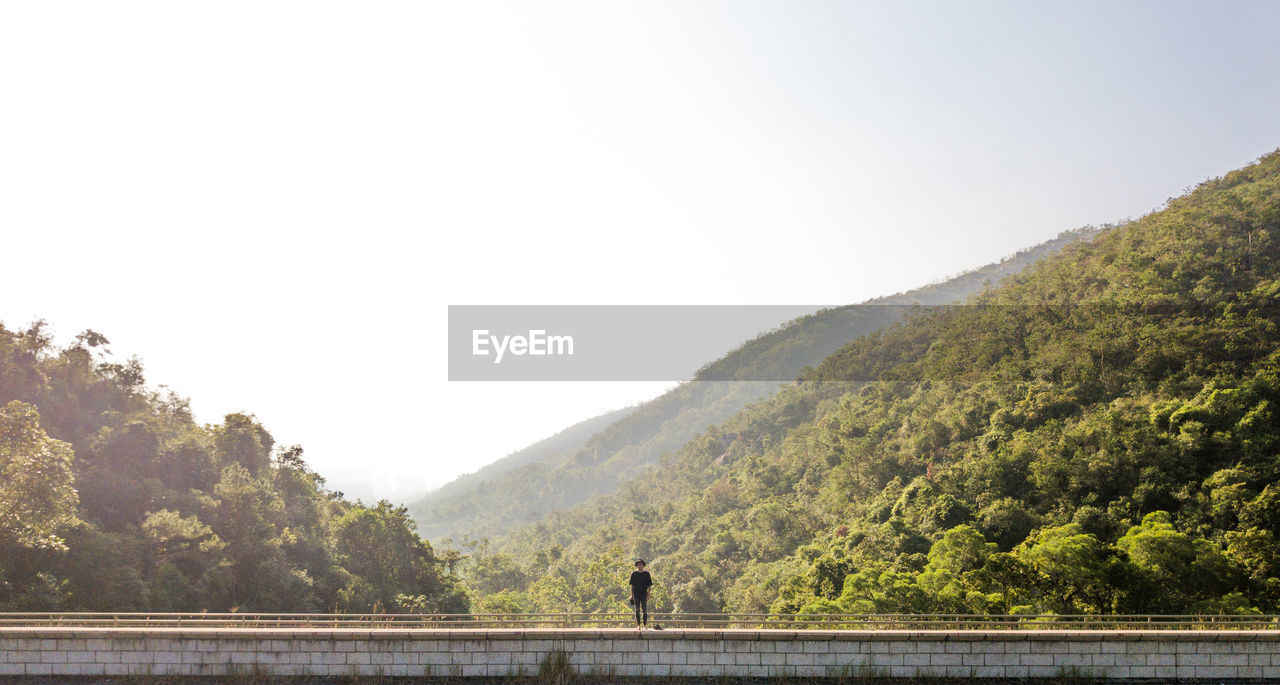 Man standing on bridge against mountains and clear sky