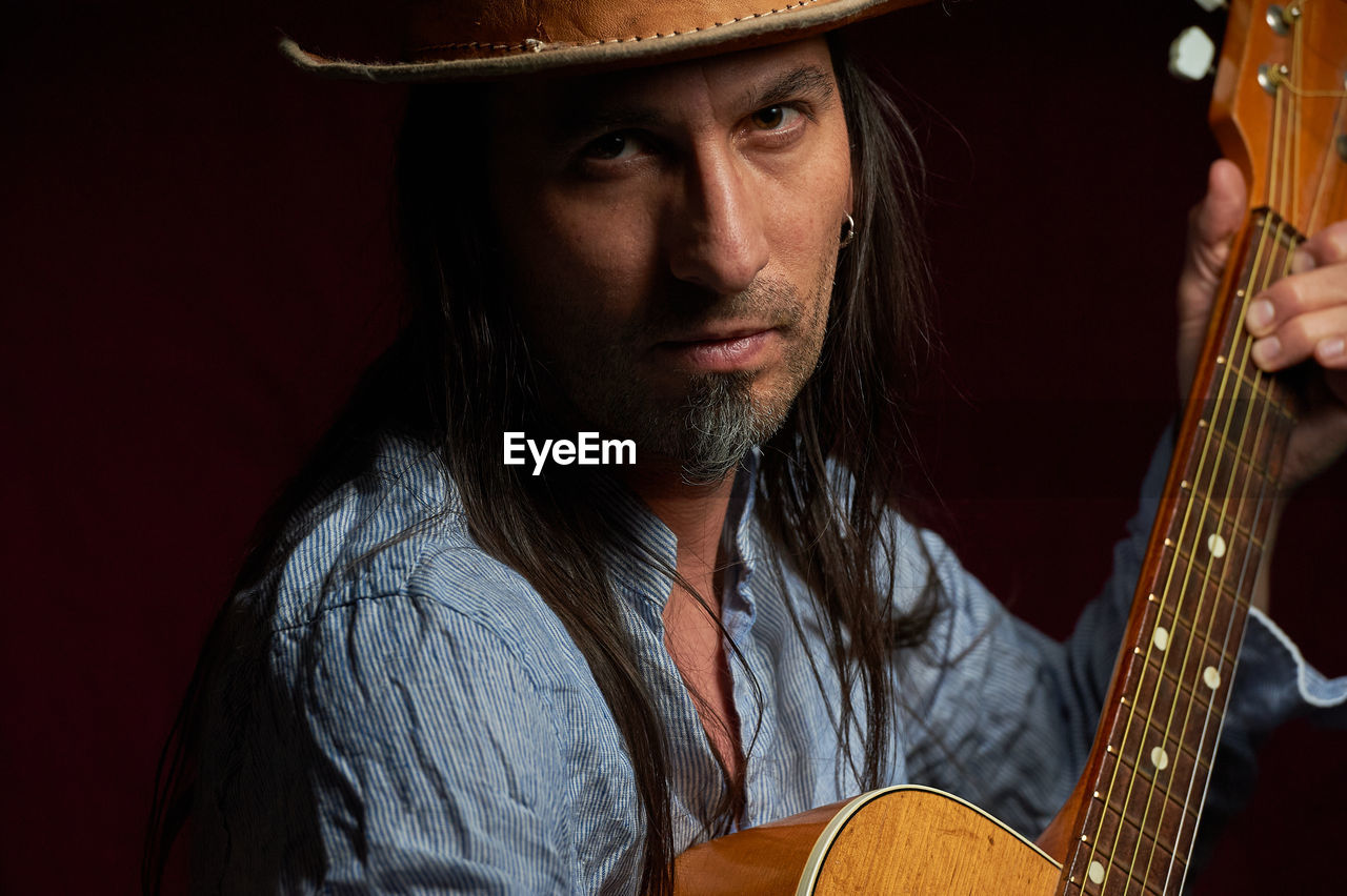 Adult musician in headshot portrait with acoustic guitar and cowboy hat