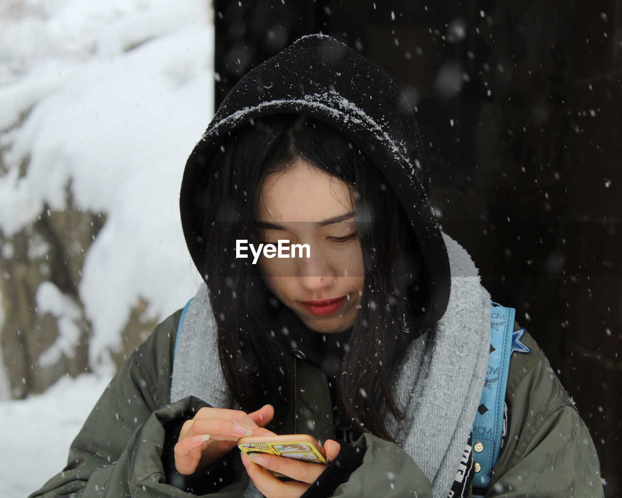 Close-up of young woman using phone during snowfall