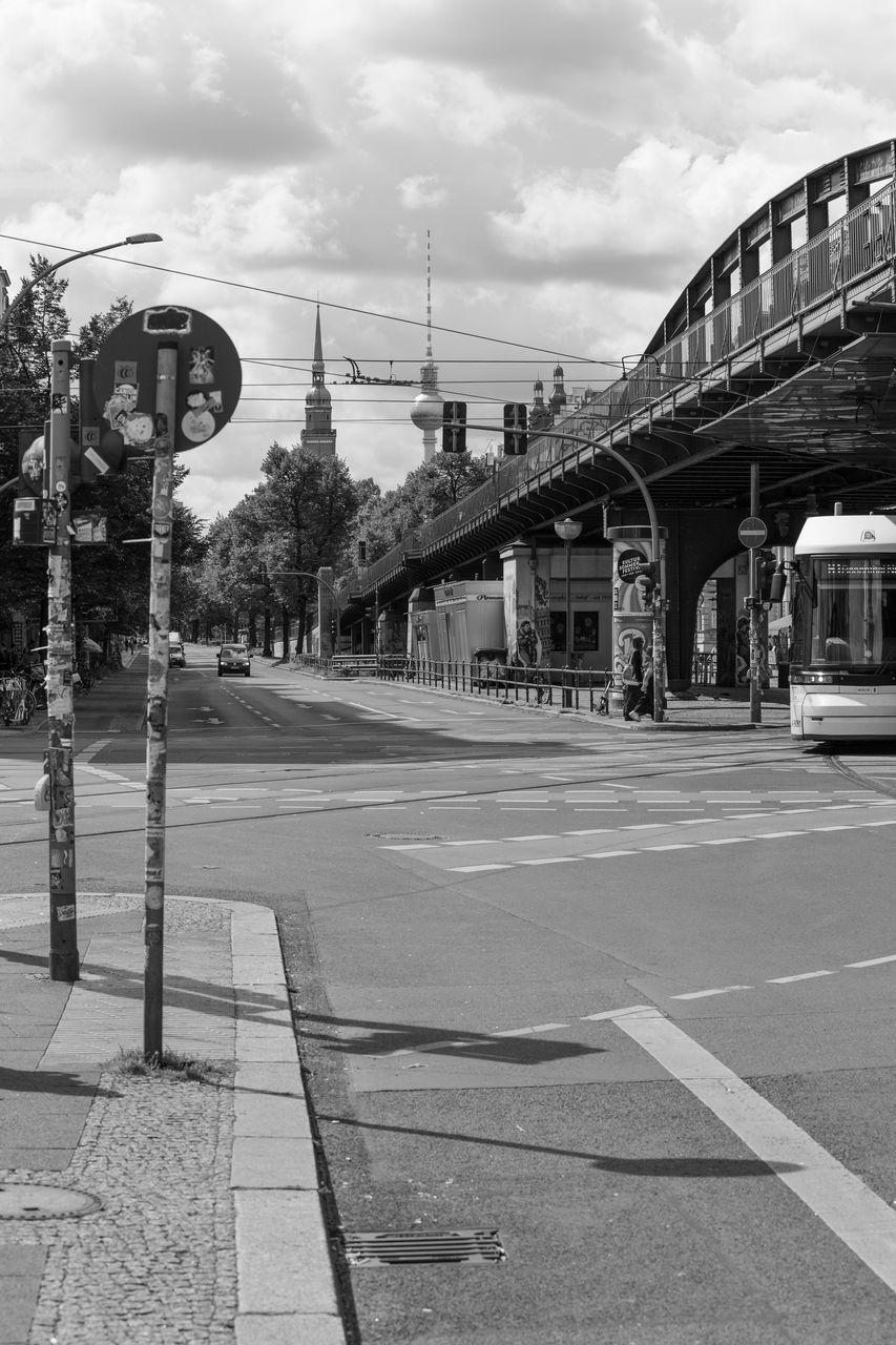 architecture, road, built structure, sky, street, transport, transportation, city, black and white, cloud, urban area, monochrome, lane, monochrome photography, nature, building exterior, infrastructure, sign, day, no people, outdoors, bridge, rail transportation, mode of transportation, symbol, tree, footpath, travel destinations, residential area, black, street light, train station, white, city street, travel, vehicle