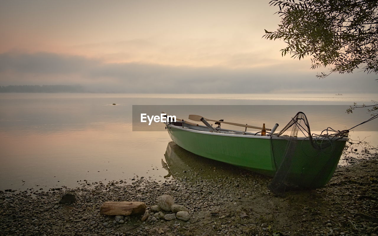 BOAT MOORED ON SEA AGAINST SKY DURING SUNSET