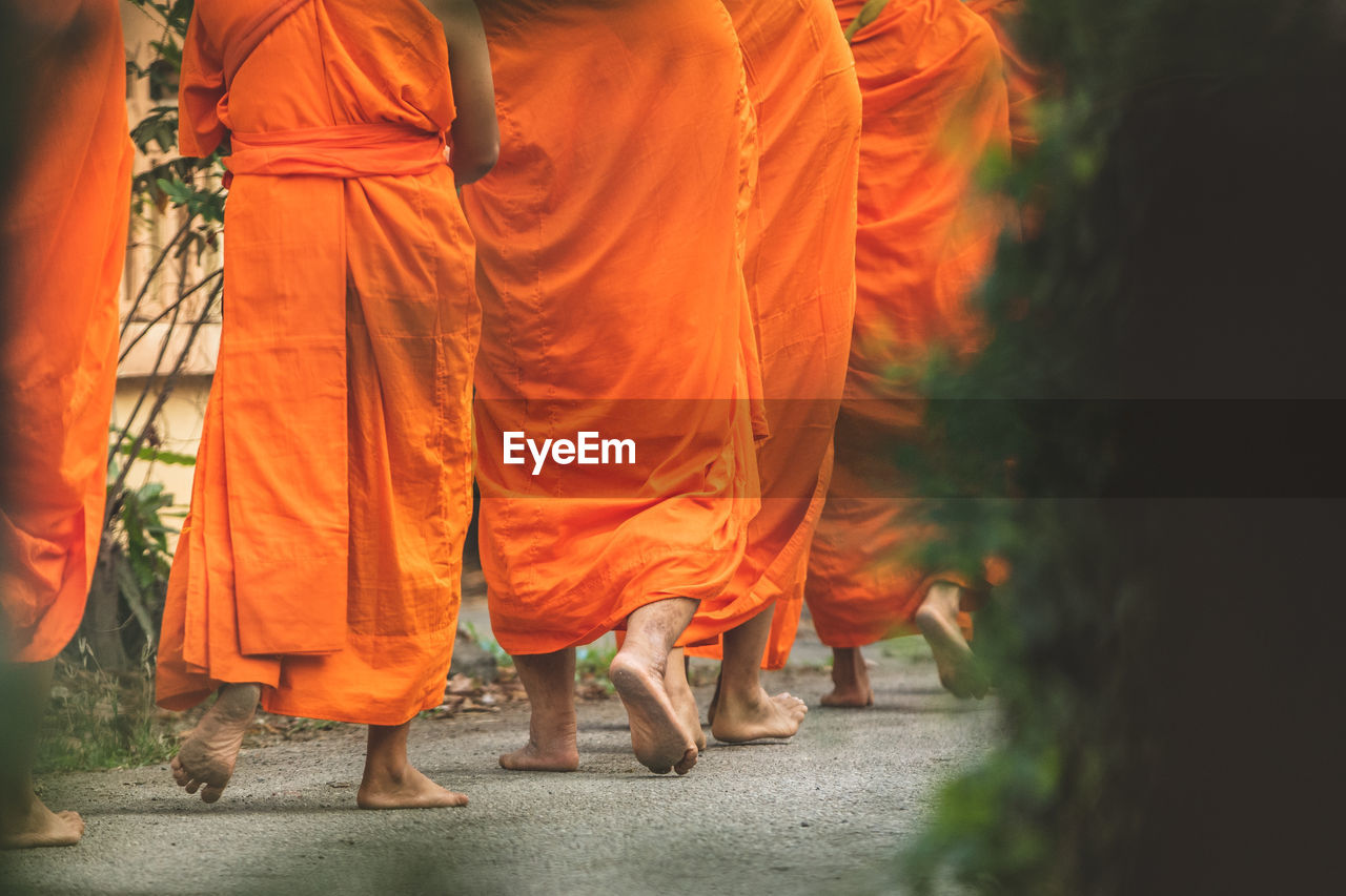 Low section of people wearing orange traditional clothing while walking on road