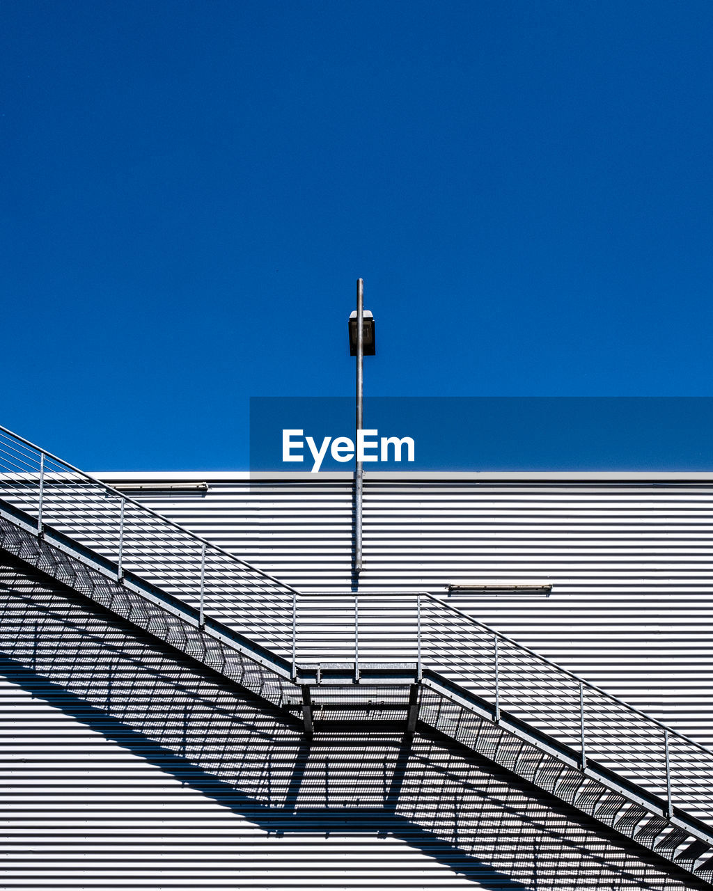 Low angle view of street light against building against clear blue sky