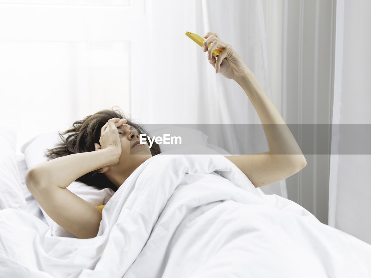 Sleepy woman looks on smartphone screen. checking e-mail box right after waking up. 