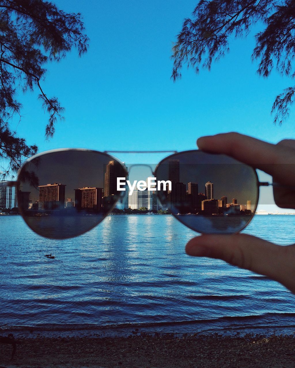 Cityscape by river seen through sunglasses held by person