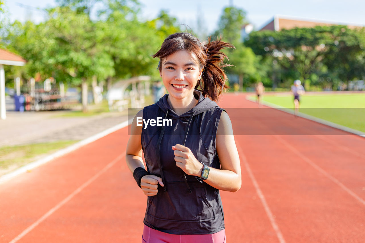 Happy beautiful young asian woman doing her running exercising at a running track on a sunny morning