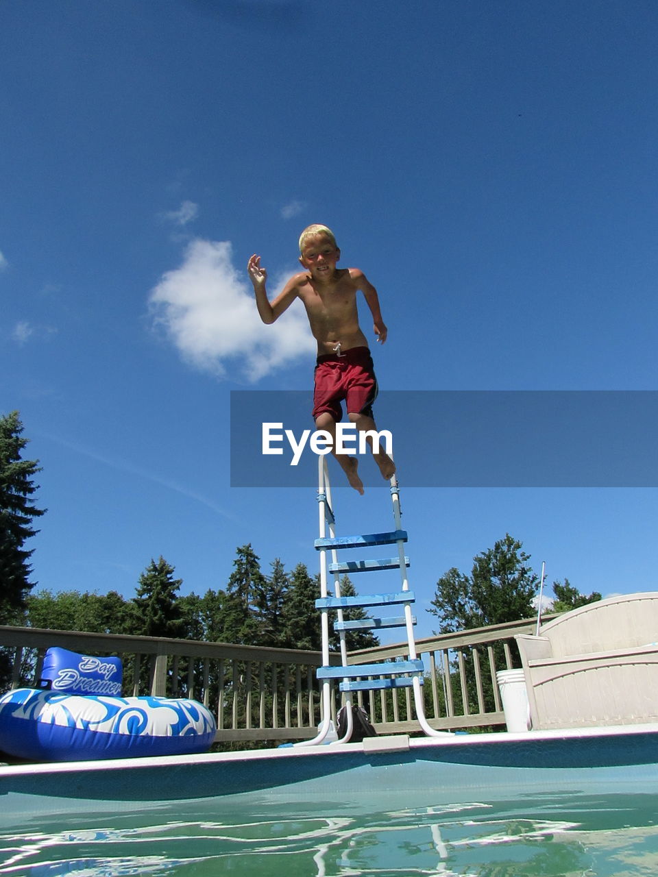 Low angle view of shirtless boy jumping in swimming pool against blue sky