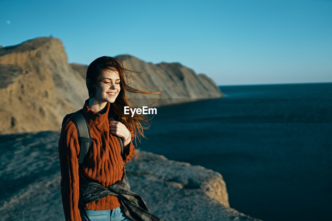 WOMAN STANDING ON ROCK AGAINST SEA