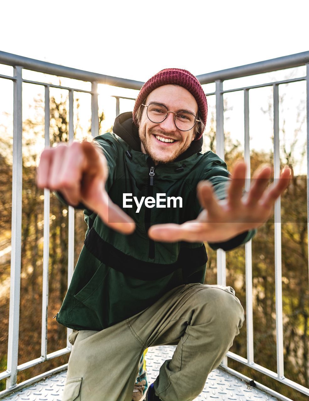 Portrait of smiling young man gesturing while kneeling against clear sky