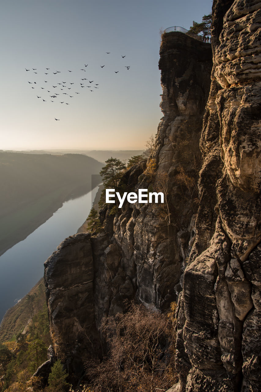 Birds flying over valley against clear sky during sunset