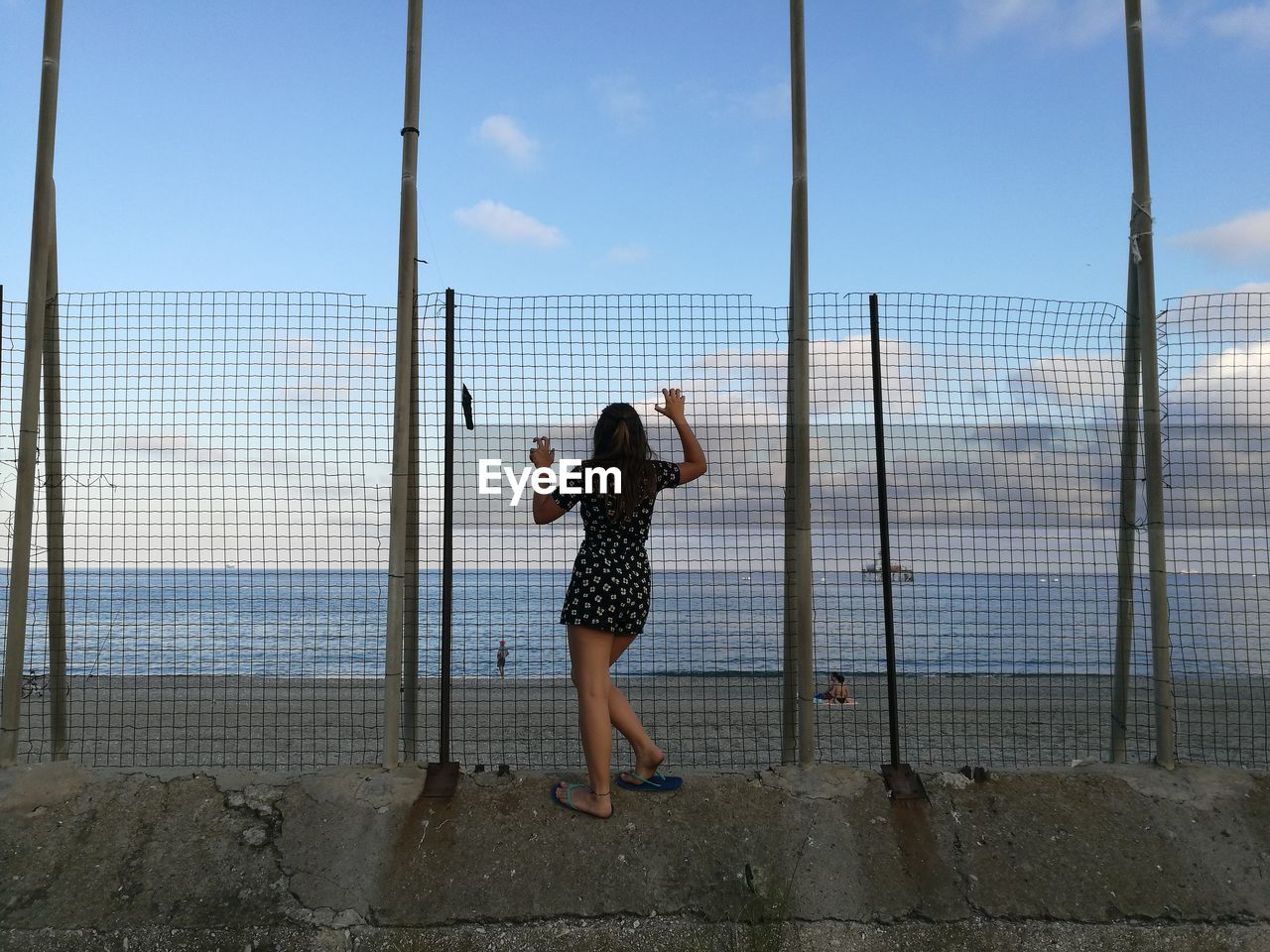 Rear view of woman looking at sea through fence 