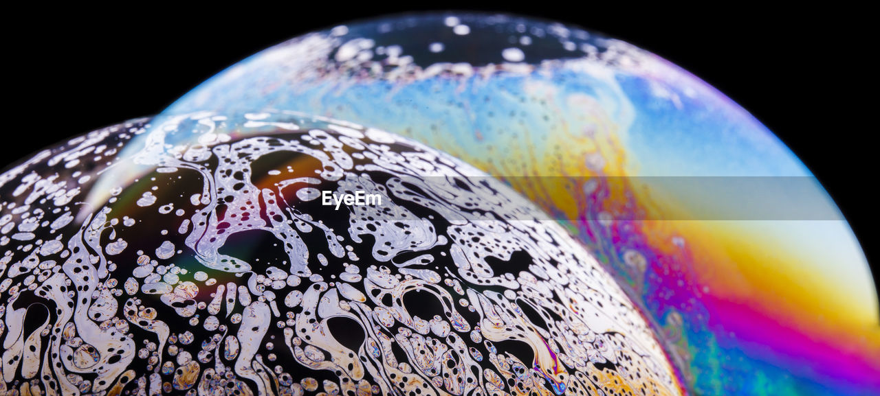 Panoramic view of closeup bubble textured backdrop representing colorful planets with wavy lines on round shaped surface on black background