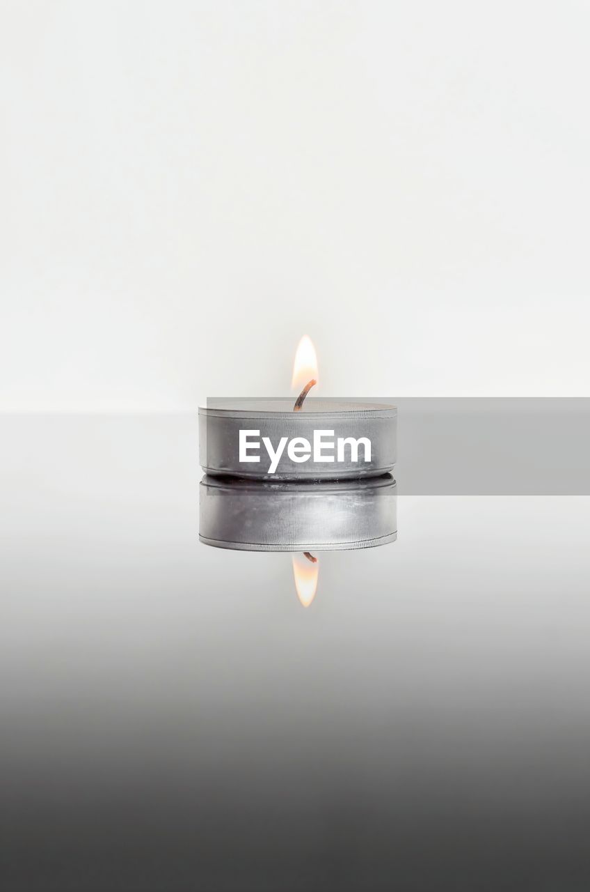 Reflection of lit tea light candle on table against white background