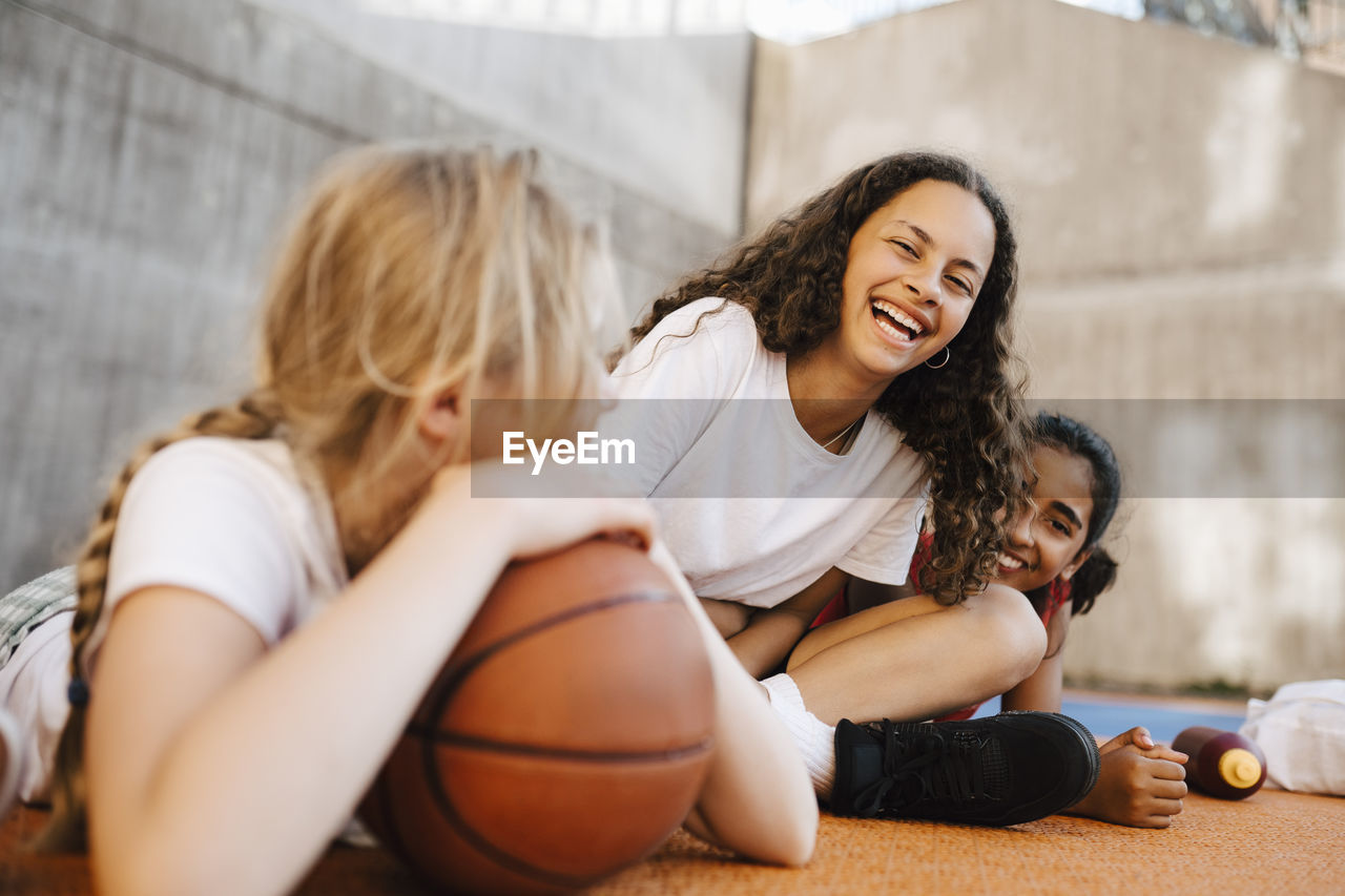 Portrait of girl laughing while sitting with female friends at basketball court