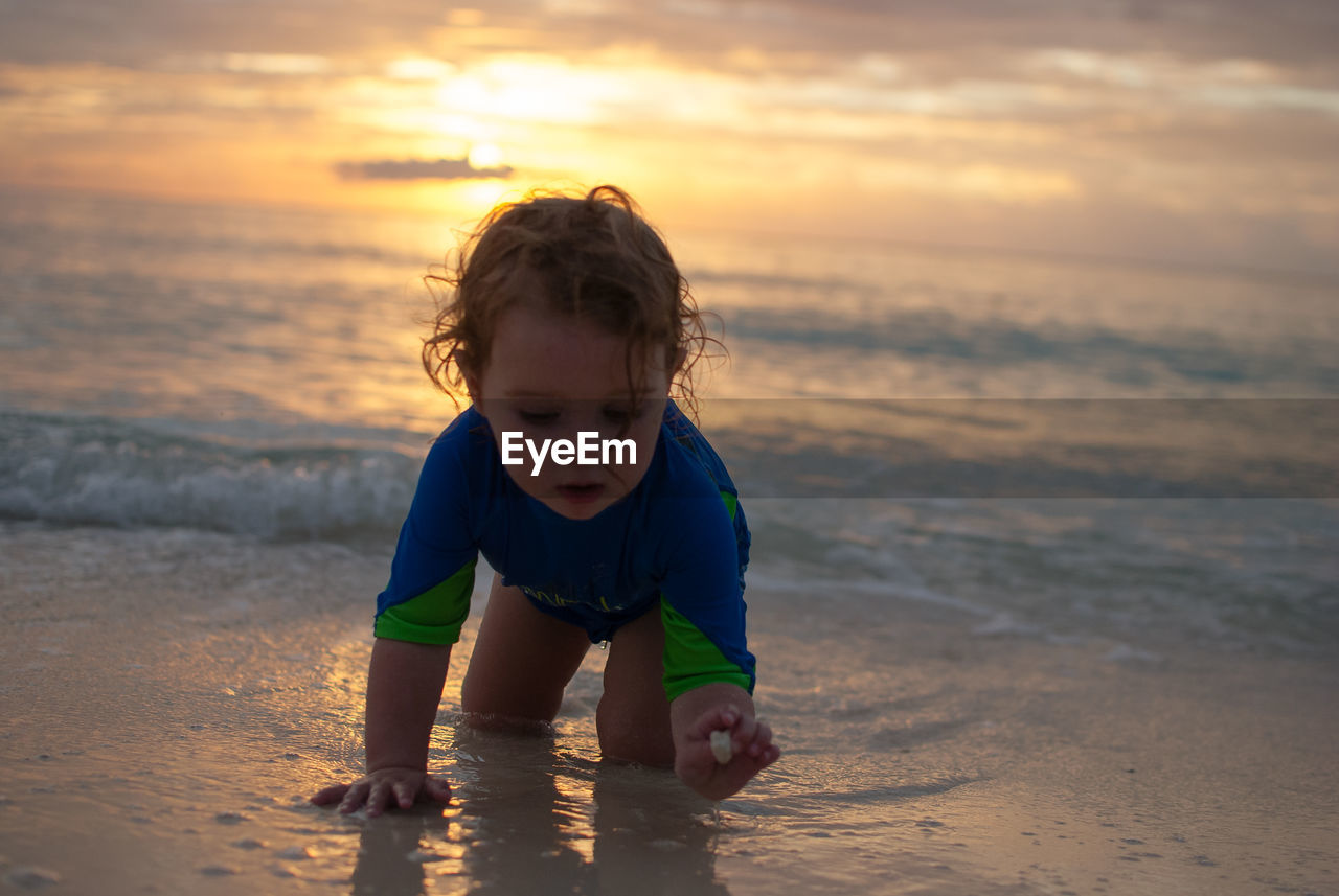 Cute girl playing at beach against sky during sunset