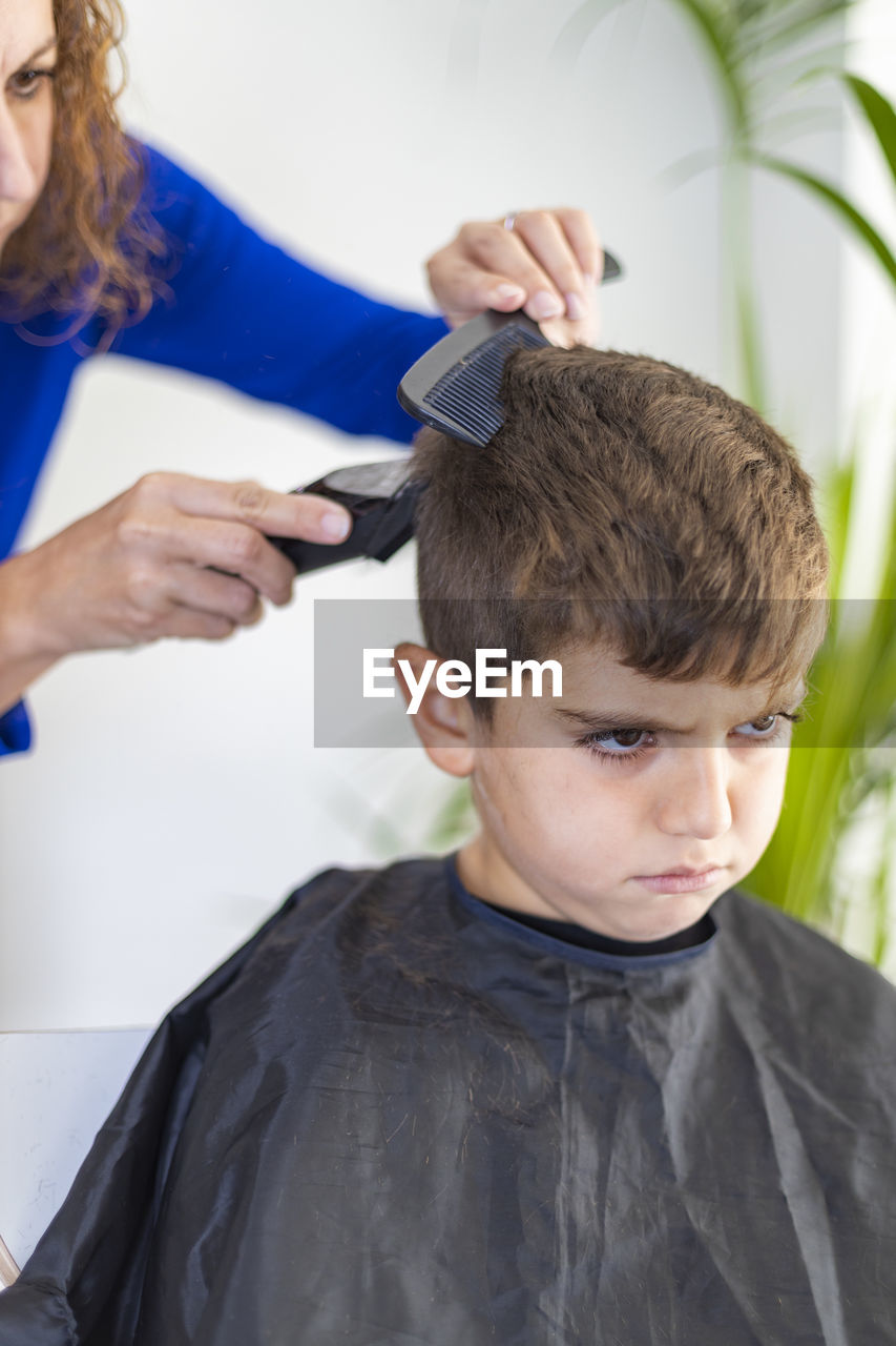 Angry boy getting haircut at home with scissors