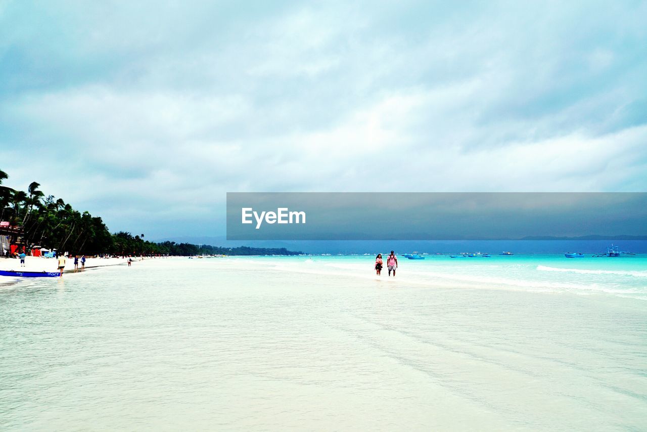 People at beach against cloudy sky