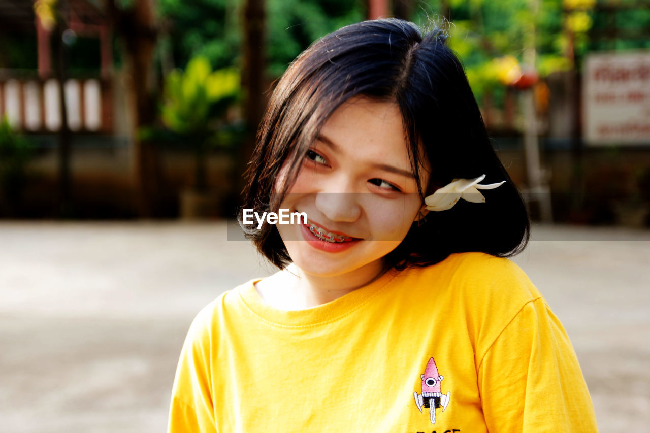 Smiling young woman wearing flower looking away outdoors
