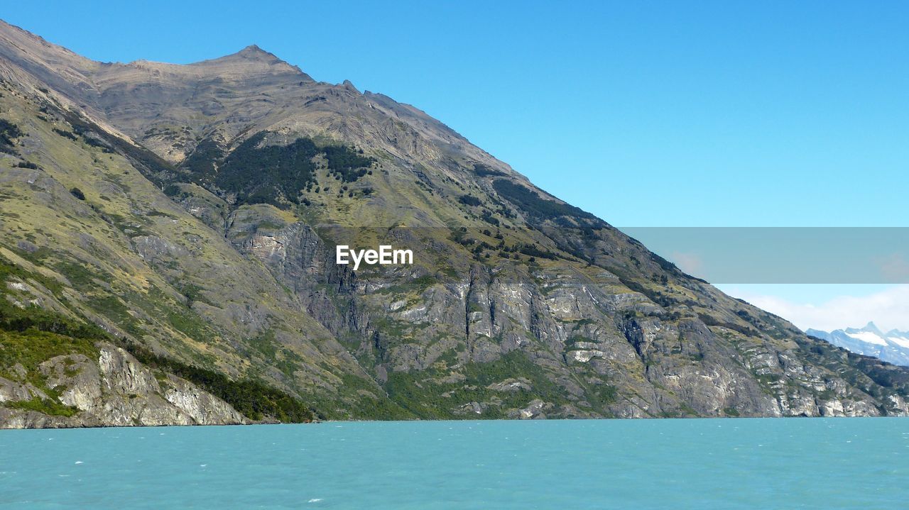 Scenic view of sea and mountains against clear blue sky