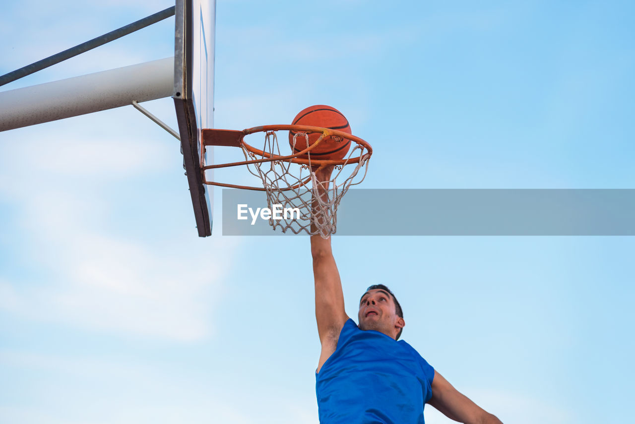 Low angle view of man playing basketball against blue sky