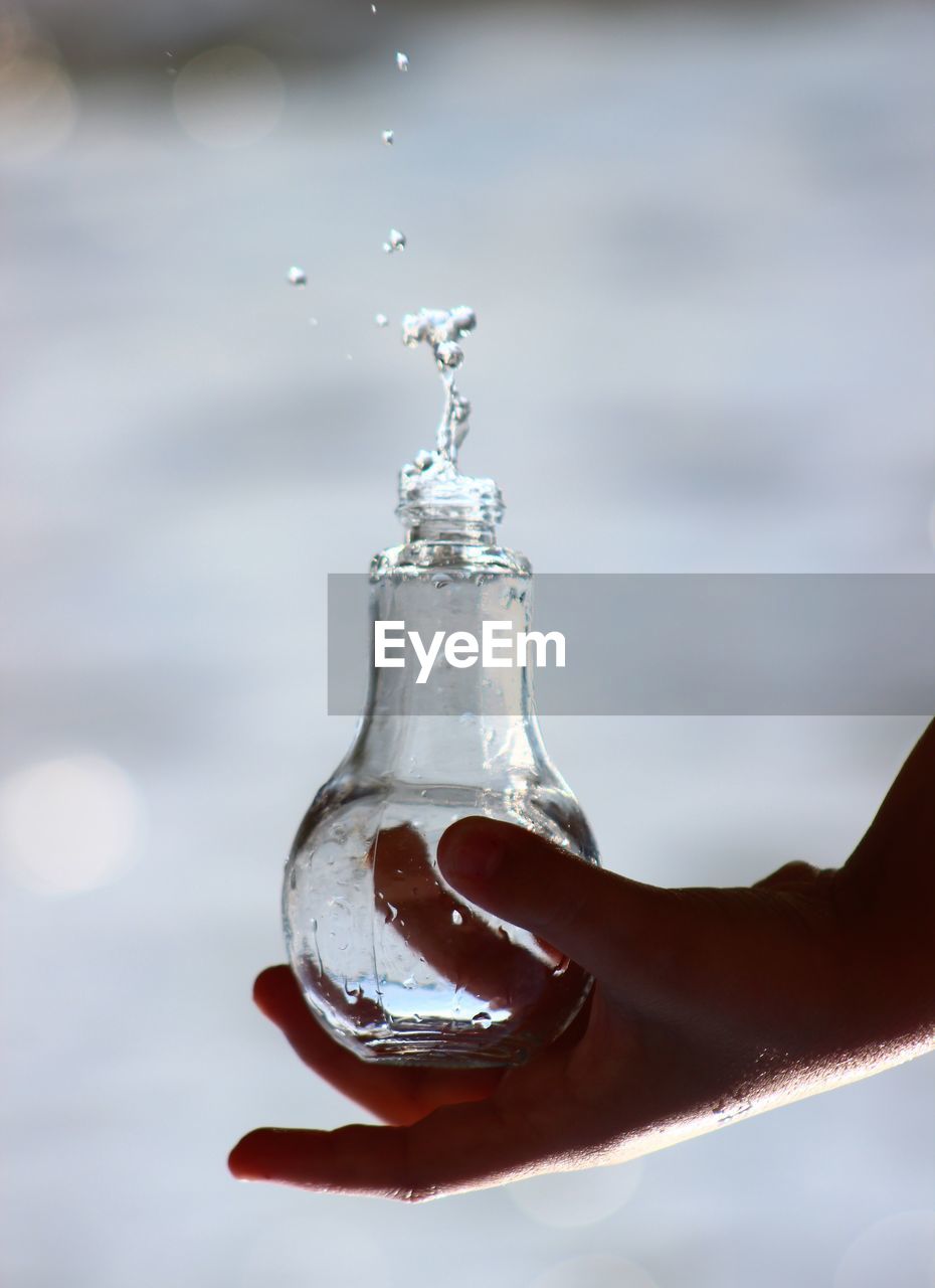 Close-up of hand holding glass bottle against blurred background