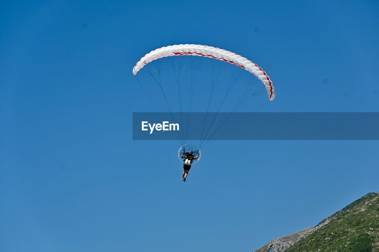 Low angle view of person paragliding against clear blue sky