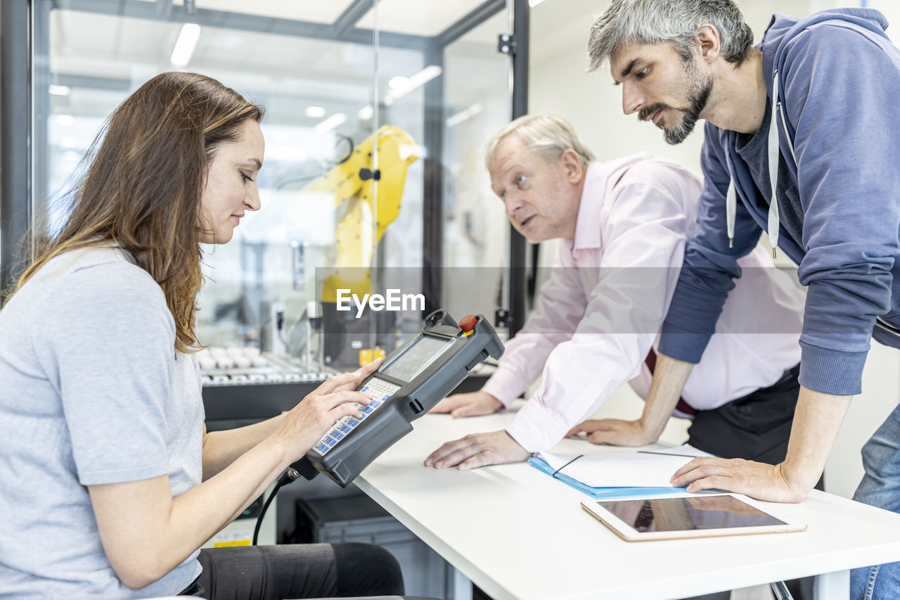 Colleagues watching woman programming robot arm with digital control