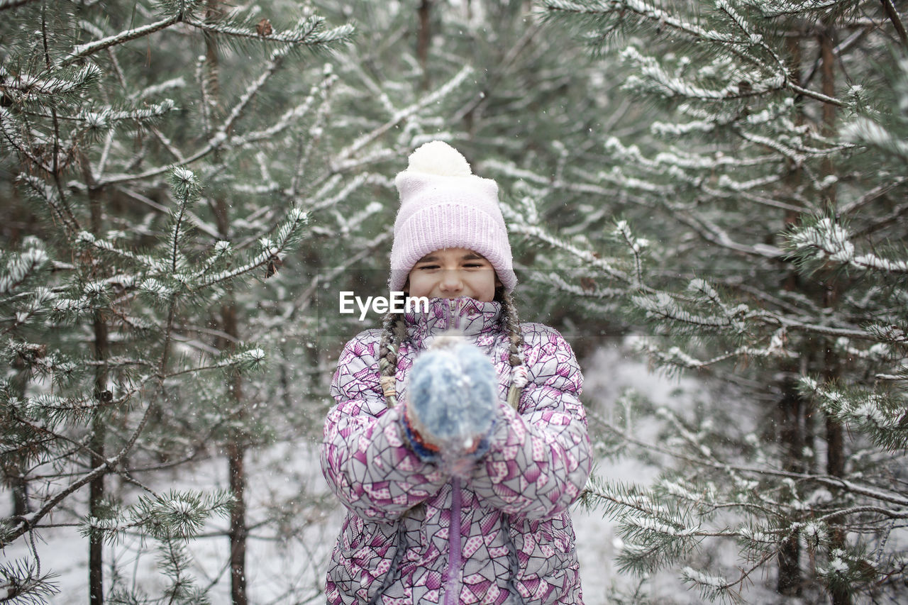 Smiling girl playing with snow against trees