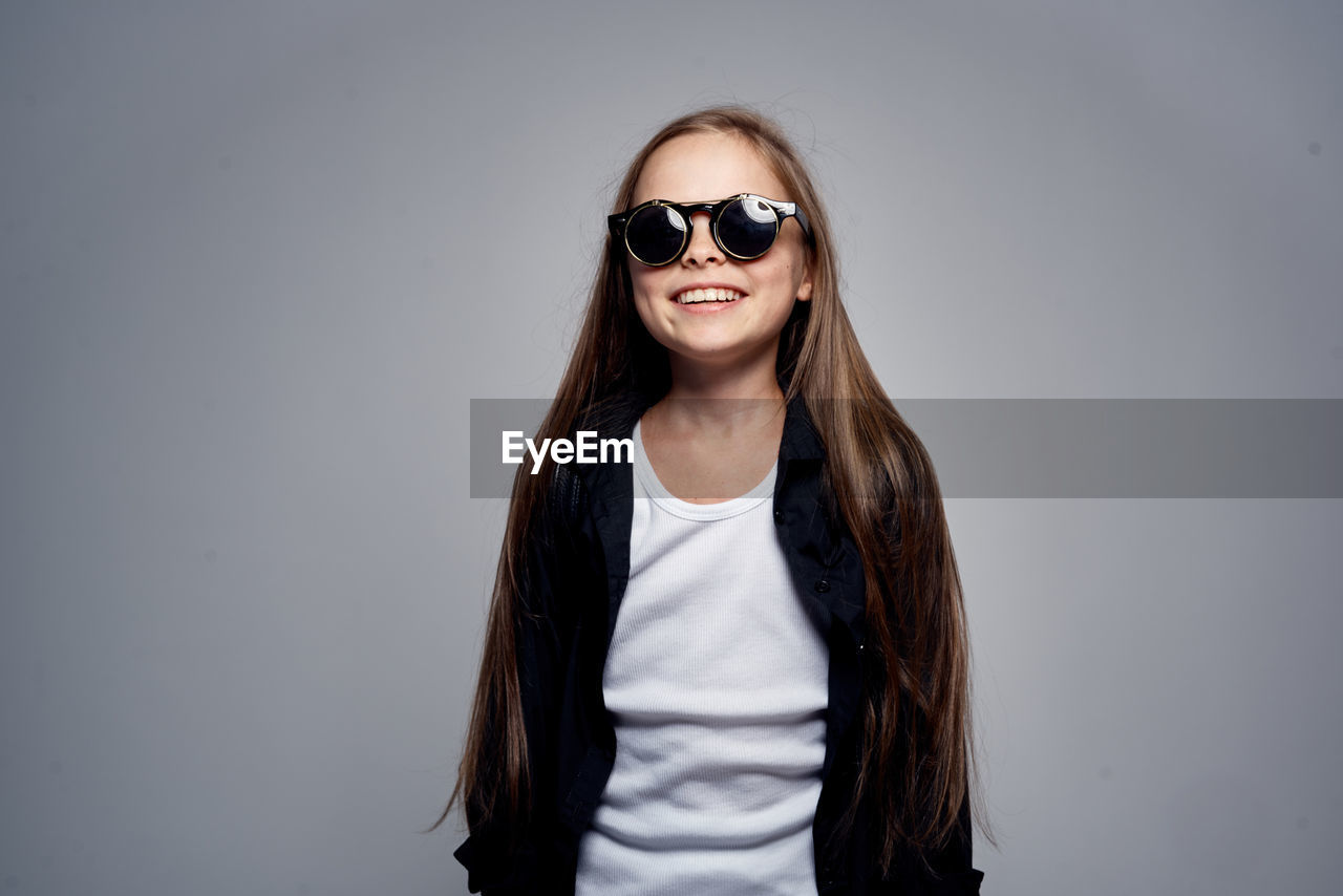 portrait of young woman wearing sunglasses while standing against white background