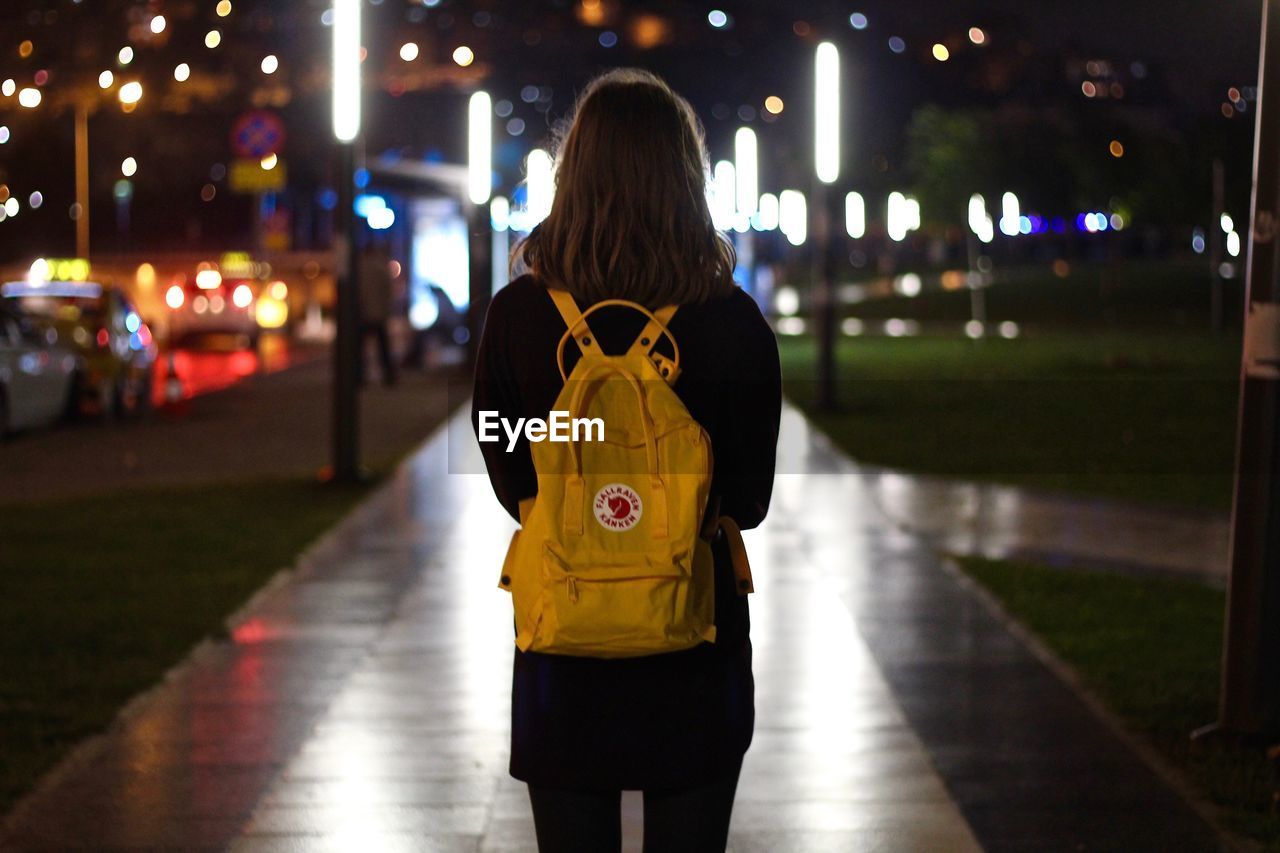 REAR VIEW OF MAN STANDING ON STREET AT NIGHT