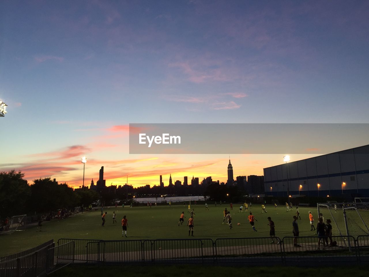 High angle view of men playing soccer on field against sky during sunset