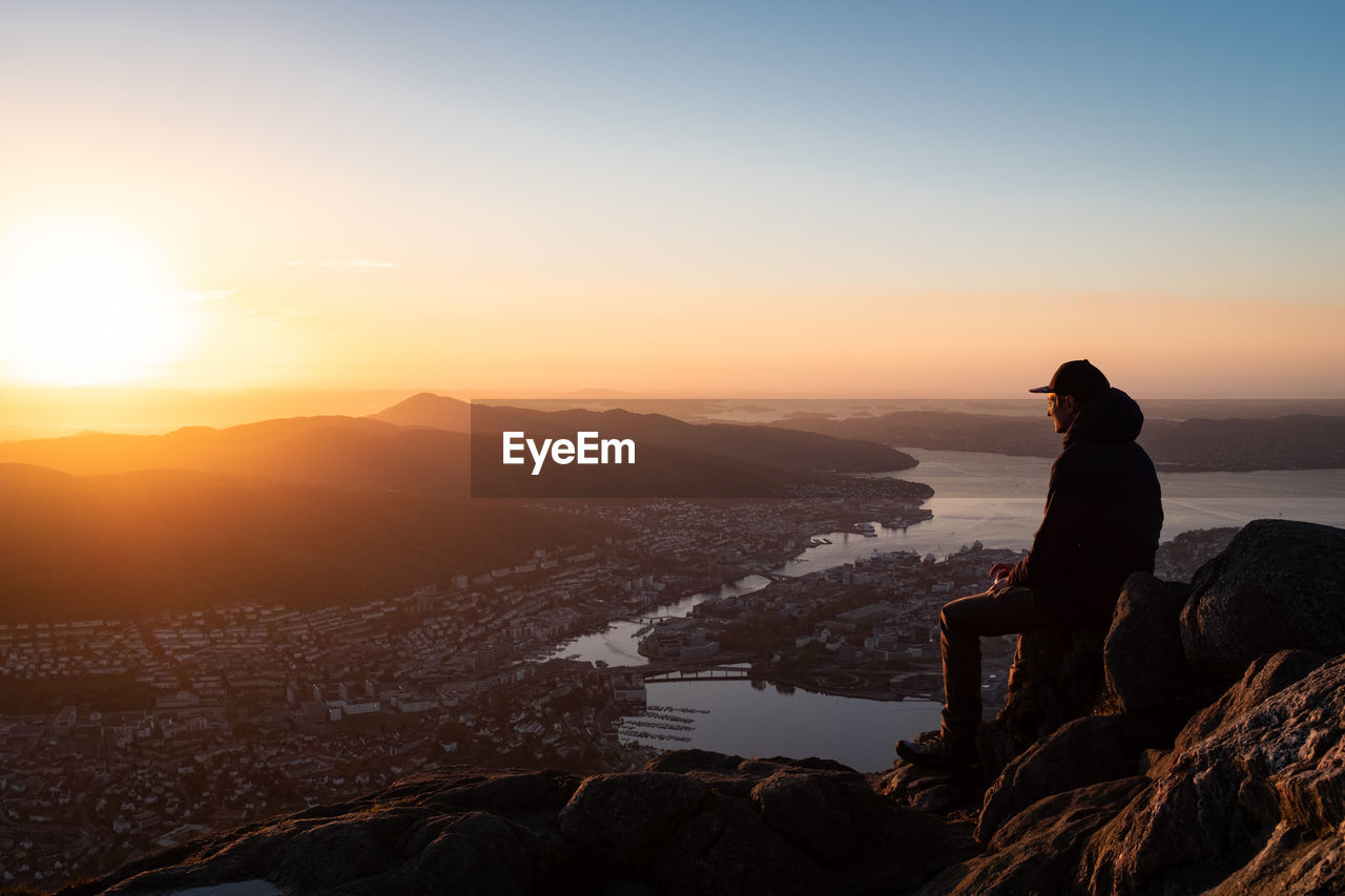 Man sitting on rock against sky at sunset