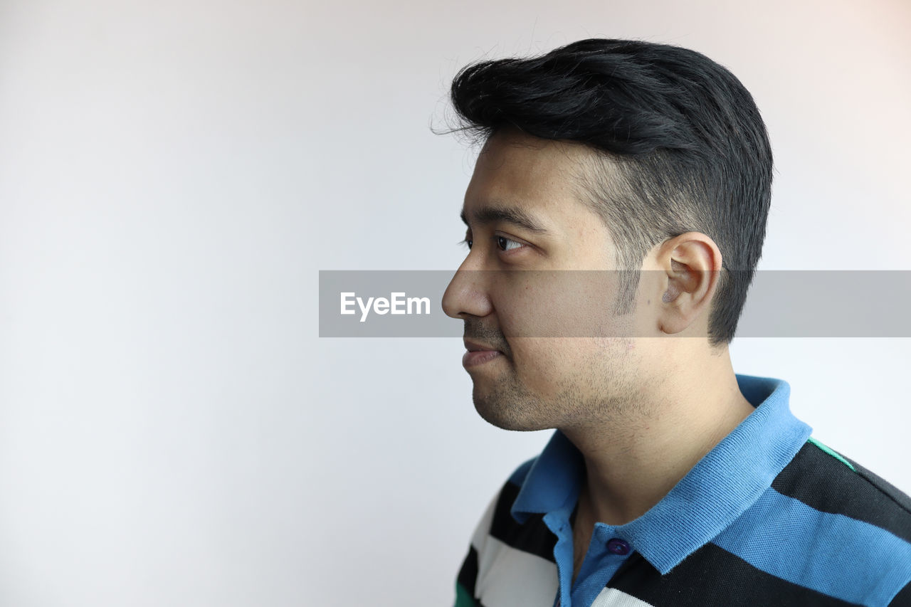 PORTRAIT OF A YOUNG MAN LOOKING AWAY AGAINST WHITE BACKGROUND