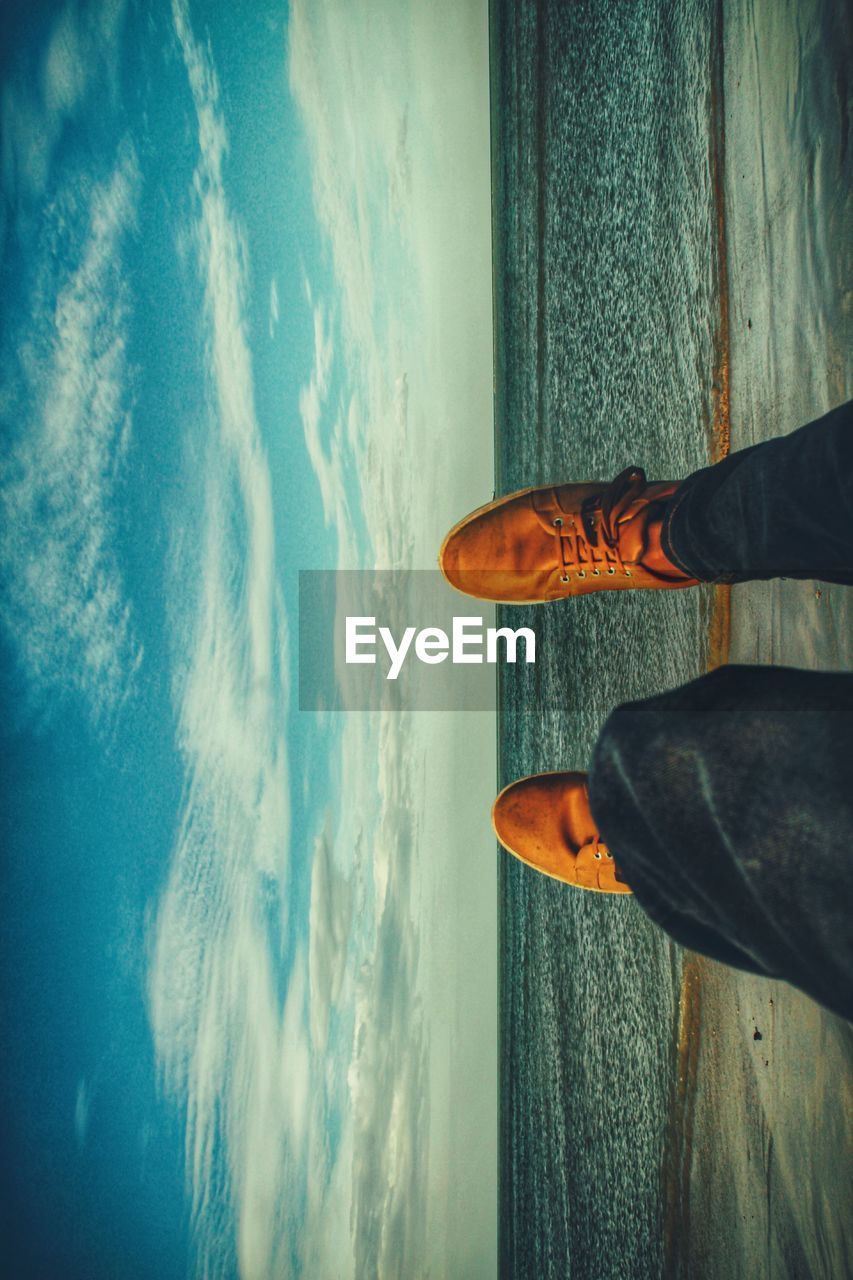 LOW SECTION OF MAN STANDING AT SEA SHORE