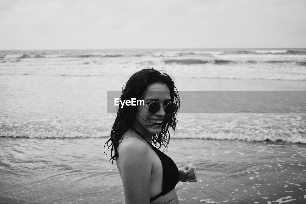 Portrait of smiling young woman in sunglasses beach against sky