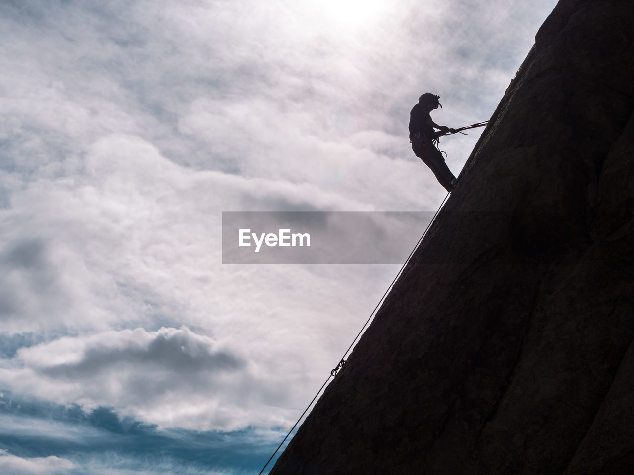 Low angle view of silhouette man climbing on mountain against sky