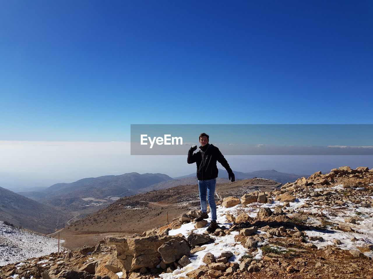 Full length of man holding snow while standing on mountain against clear blue sky