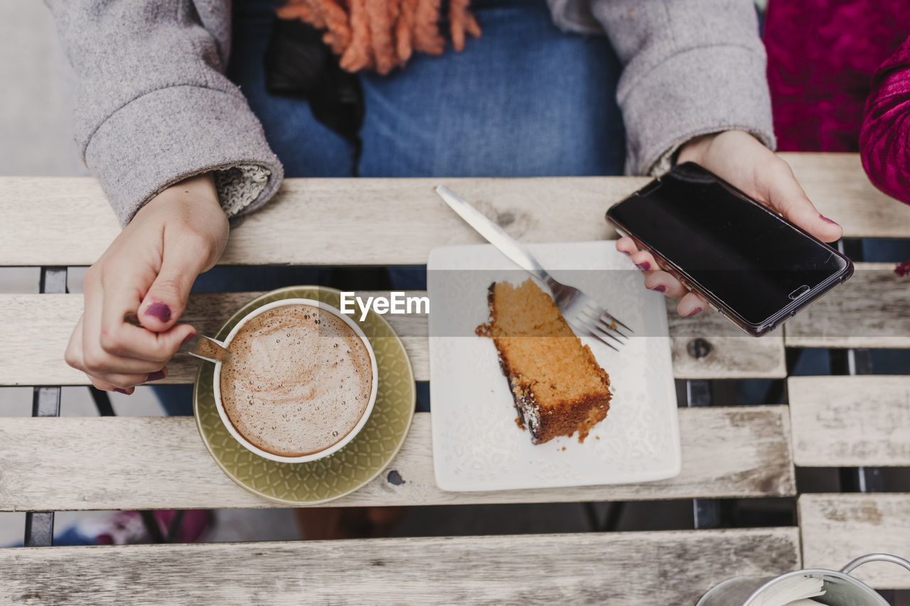 MIDSECTION OF WOMAN HOLDING COFFEE CUP ON TABLE AT BEACH