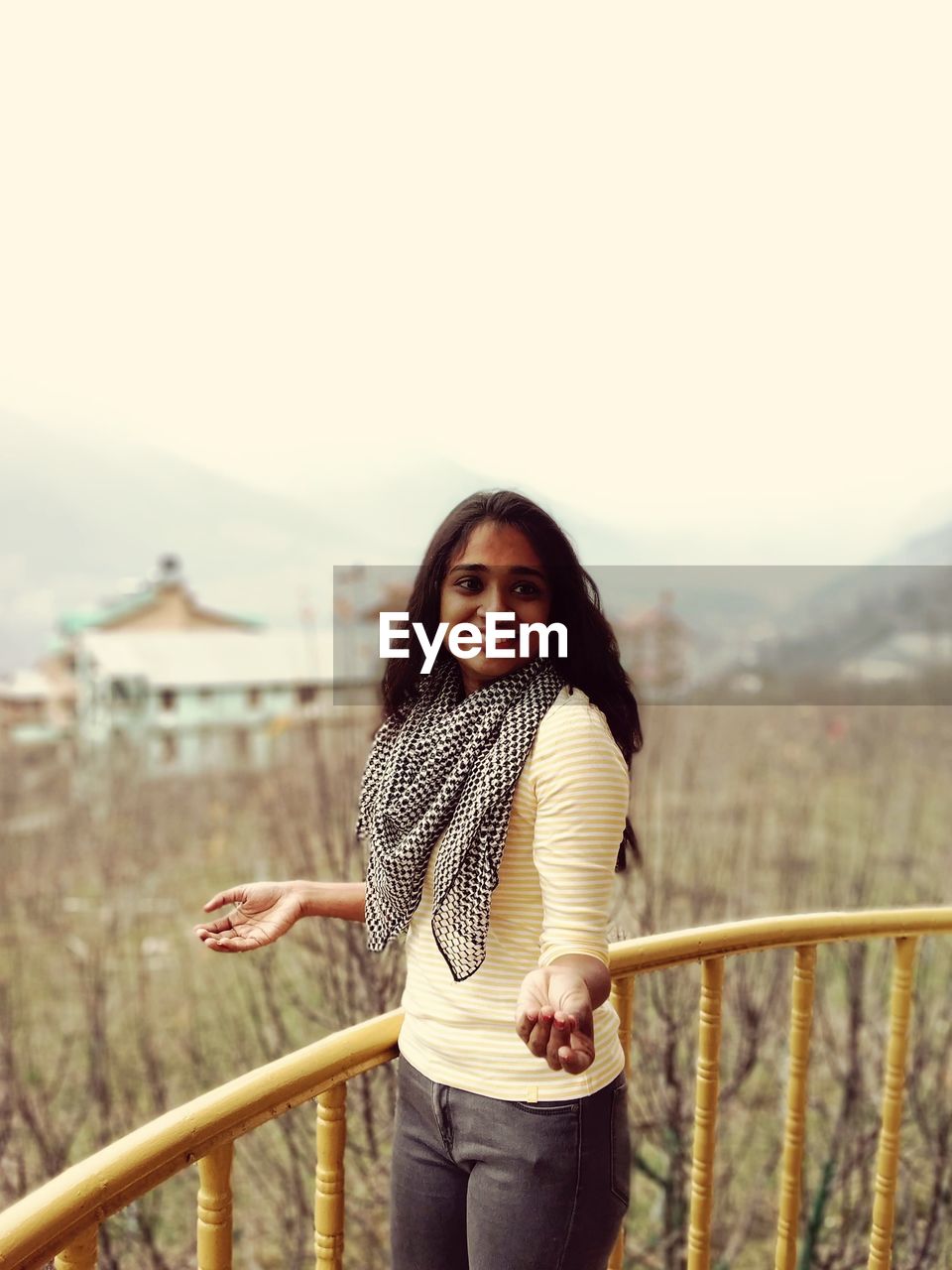 PORTRAIT OF SMILING WOMAN STANDING AGAINST RAILING