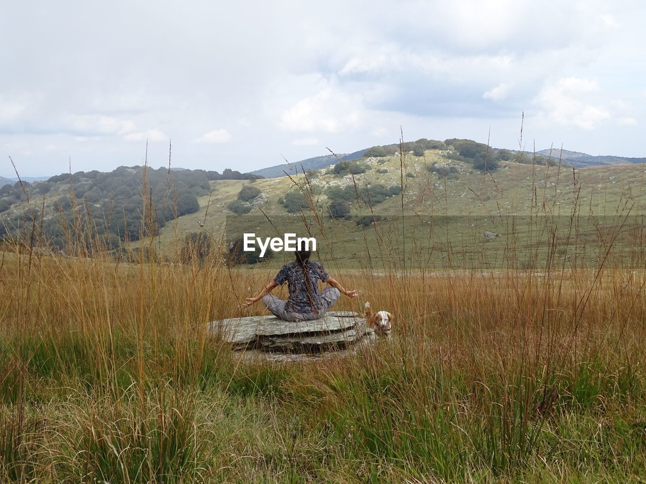 Rear view of woman exercising on rock against sky