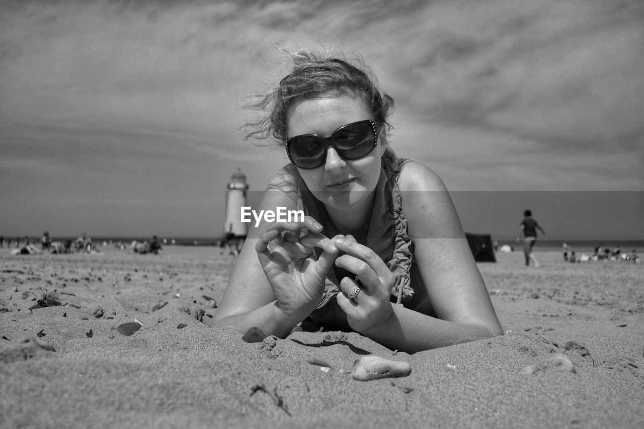 PORTRAIT OF WOMAN HOLDING SUNGLASSES AT BEACH